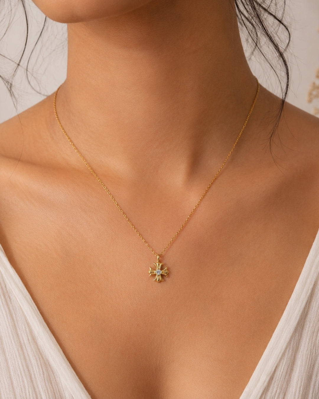 A delicate gold chain necklace with a small starburst pendant featuring light green and white accents, worn by a model in a close-up shot.