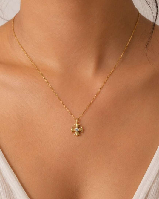 A delicate gold chain necklace with a small starburst pendant featuring light green and white accents, worn by a model in a close-up shot.