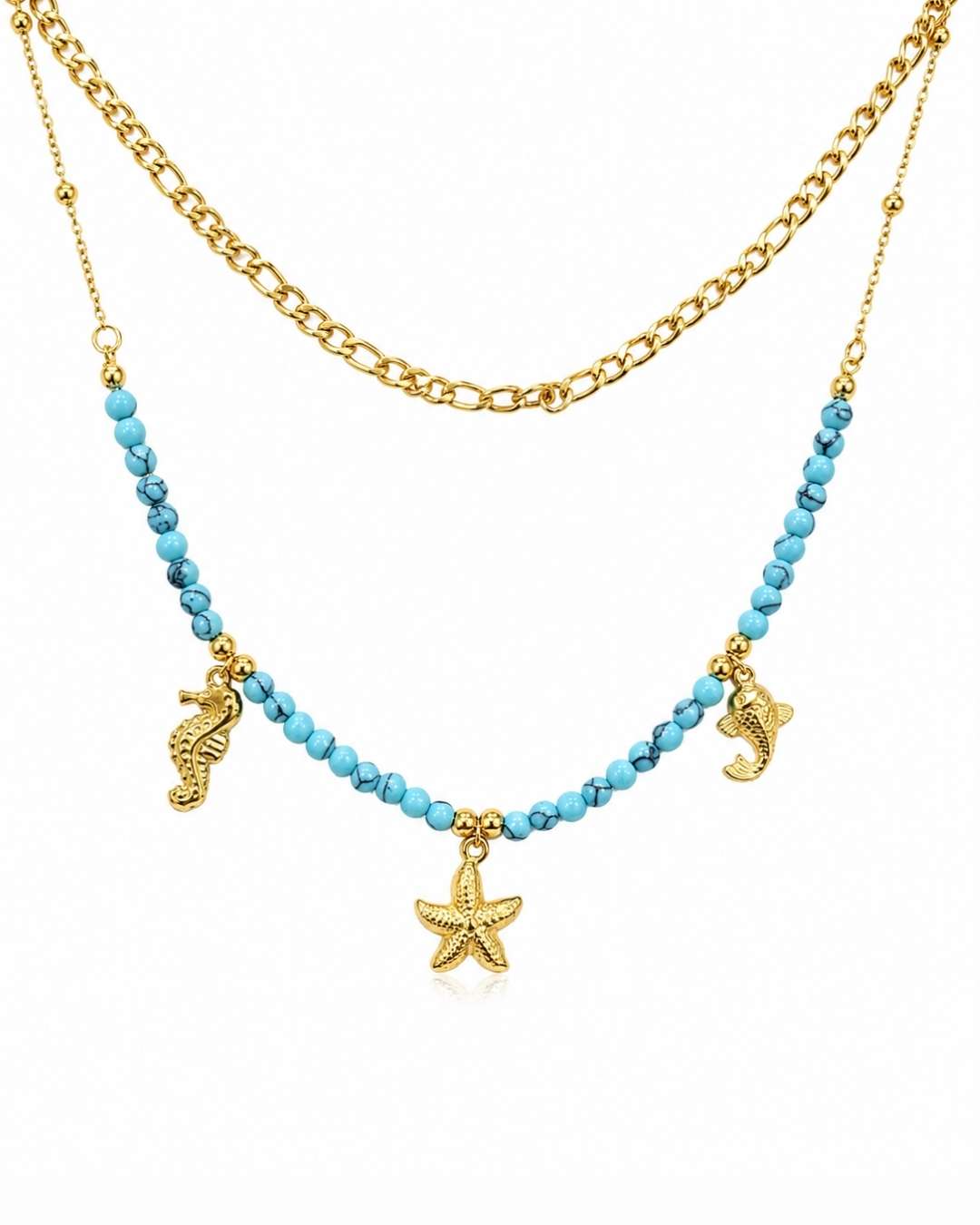 A double-layered necklace featuring a gold chain and a beaded strand of light blue beads with gold sea-themed charms, including a starfish, seahorse, and dolphin, on a white background.