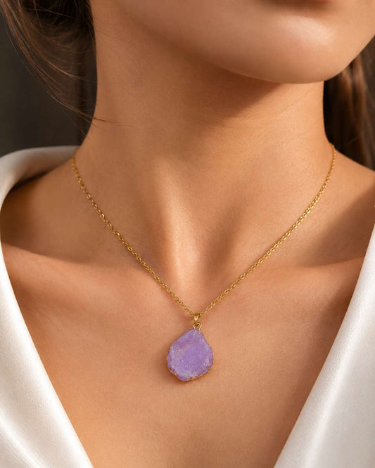 A gold chain necklace with a teardrop-shaped light purple daisy-cut gemstone pendant, shown worn on a model's neck.