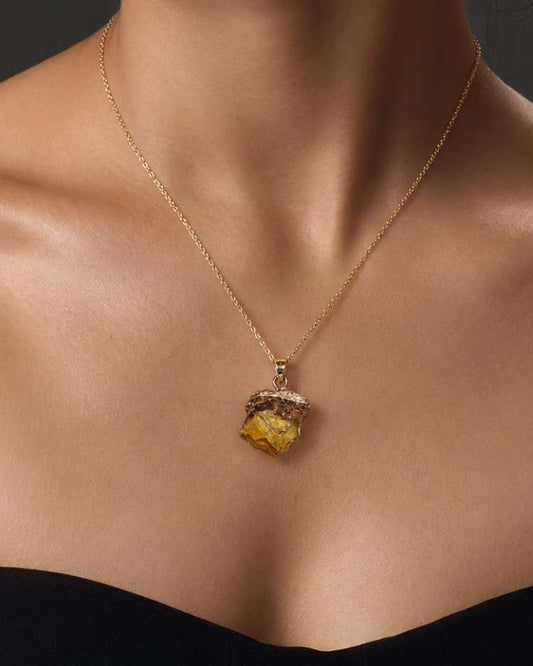 A close-up of a model wearing a delicate gold chain necklace with a textured, organic-shaped yellow gemstone pendant.