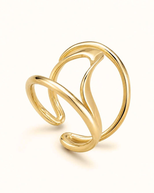 A polished gold abstract wrap ring with a fluid, flowing design, photographed on a clean off-white background.
