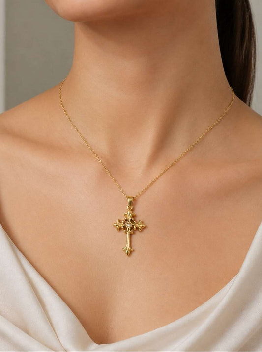 A close-up of a model wearing a delicate gold cross pendant necklace with a fine chain, styled with a white satin top.