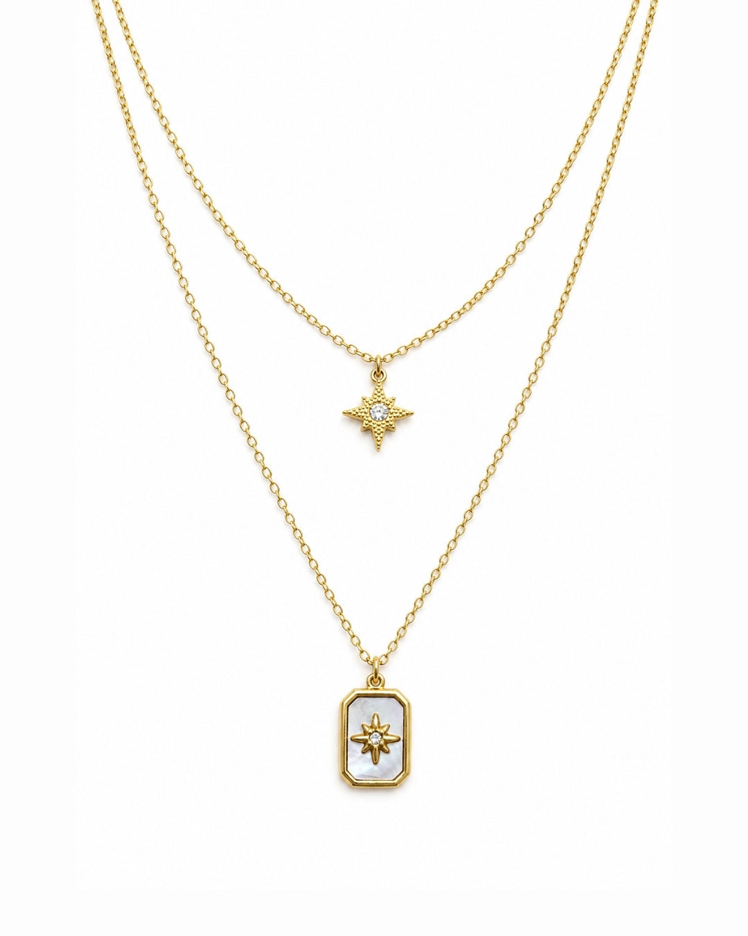 A double-layered gold necklace set on a white background. The shorter chain features a small gold starburst pendant with a clear stone, while the longer chain features a gold rectangular pendant with a white inlay and a gold sunburst design in the center.