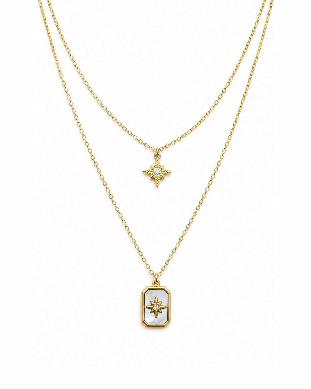 A double-layered gold necklace set on a white background. The shorter chain features a small gold starburst pendant with a clear stone, while the longer chain features a gold rectangular pendant with a white inlay and a gold sunburst design in the center.