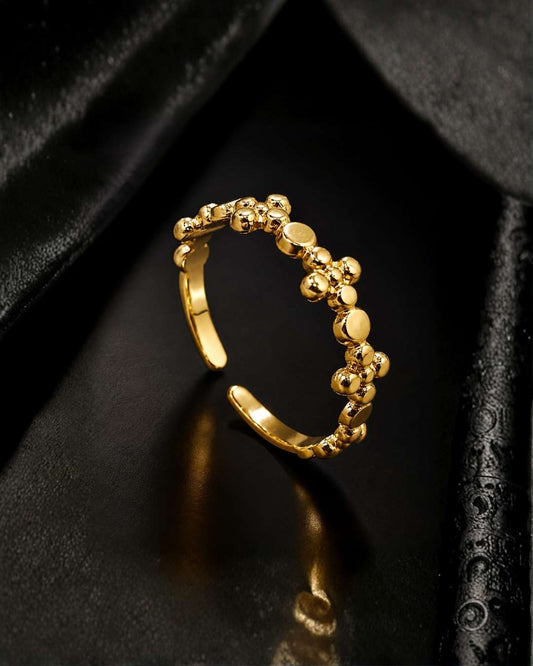 A gold adjustable ring with a textured, beaded floral pattern, displayed on a black satin surface.