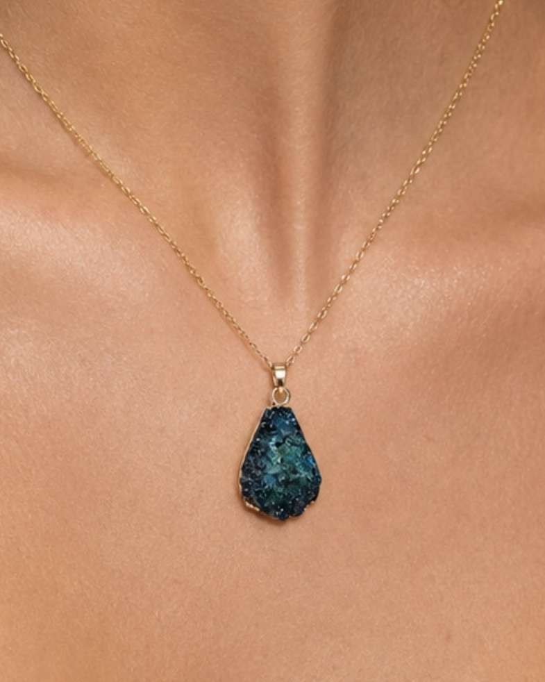 A gold chain necklace with a teardrop-shaped dark blue textured stone pendant, worn on a model's neck.