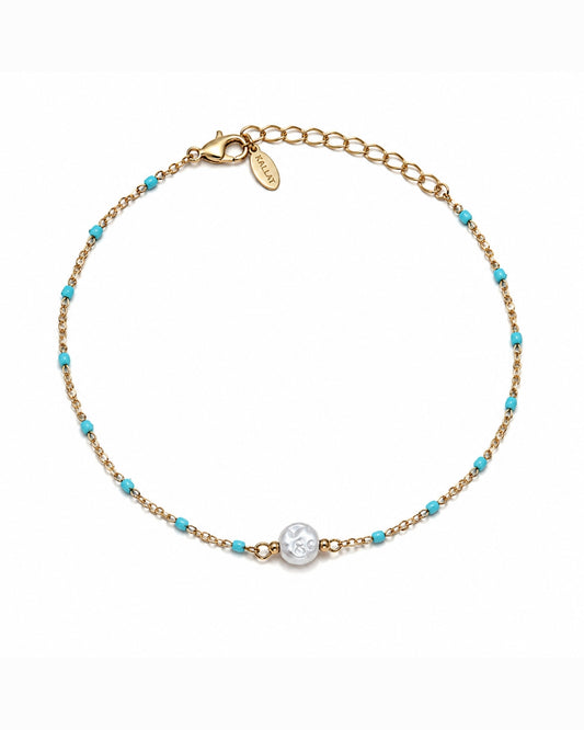 A delicate gold chain bracelet with small turquoise blue beads and a central round silver-toned charm, displayed on a clean white background.