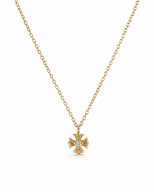 A delicate gold chain necklace featuring a small gold cross pendant with a central clear gemstone, displayed against a solid white background.