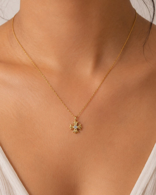 A delicate gold chain necklace with a small starburst pendant featuring light green and white accents, worn by a model in a close-up shot.