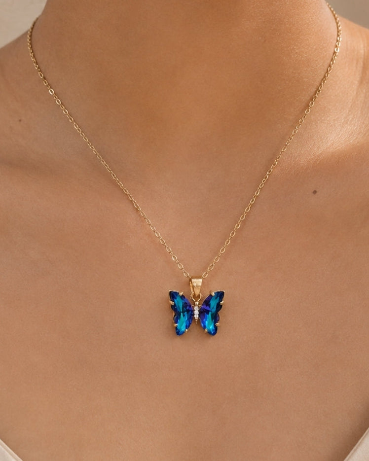A gold chain necklace with a butterfly pendant featuring blue and purple crystals, worn by a model.