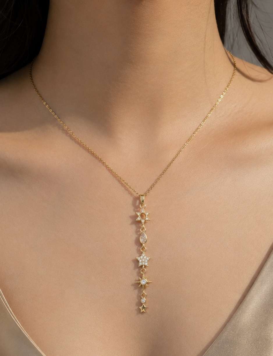 A close-up of a model wearing a delicate gold Y-necklace with a vertical drop of star-shaped charms, some embellished with small clear stones.