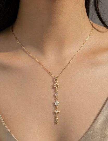 A close-up of a model wearing a delicate gold Y-necklace with a vertical drop of star-shaped charms, some embellished with small clear stones.