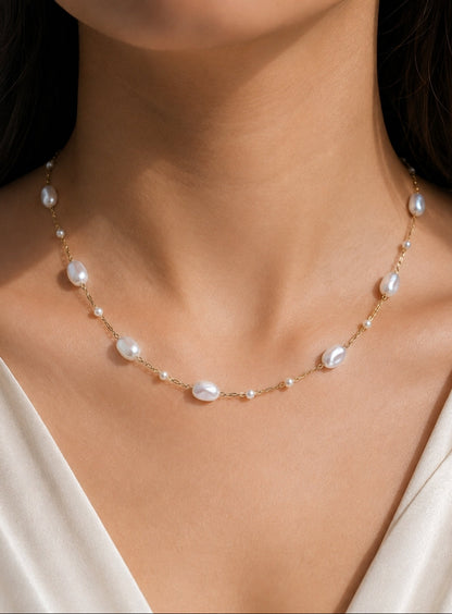 A delicate gold chain necklace featuring irregular white baroque pearls and small pearl-like beads, shown worn on a model's neck.