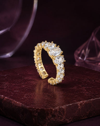 A yellow gold eternity ring set with round brilliant-cut diamonds, displayed on a dark brown marble block against a dark purple background.