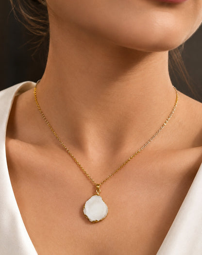 A close-up of a model wearing a delicate gold chain necklace with a large, irregular white stone pendant.