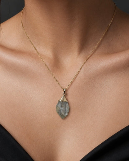 A close-up of a model wearing a delicate gold chain necklace with a teardrop-shaped gray stone pendant.
