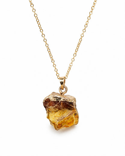 A gold chain necklace featuring a raw, rough-cut amber crystal pendant with a gold bezel setting, shown against a plain white background.