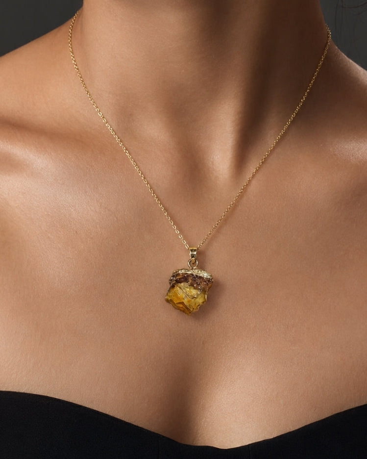 A close-up of a model wearing a delicate gold chain necklace with a textured, organic-shaped yellow gemstone pendant.
