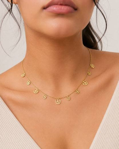 A close-up of a model wearing a delicate gold chain necklace with multiple small peace sign charms.
