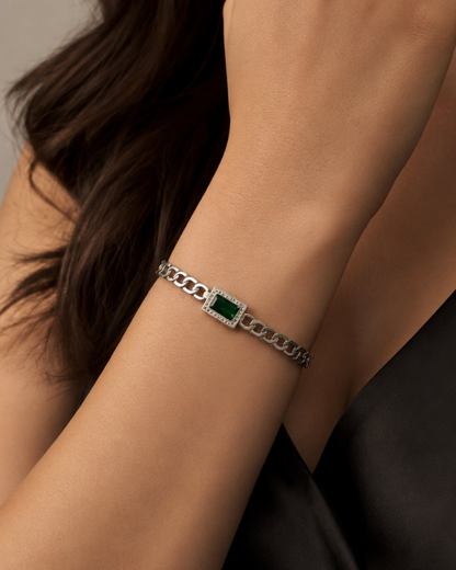 A silver chain bracelet with a central rectangular green stone, worn on a woman's wrist against a dark top and neutral background.
