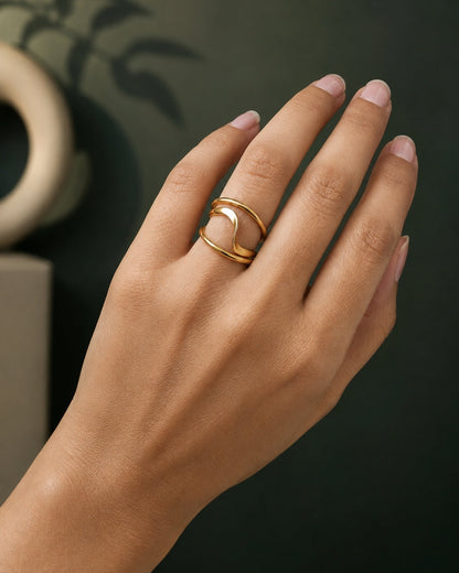 A close-up of a hand wearing a gold ring with a crescent moon design, set against a dark, softly blurred background.