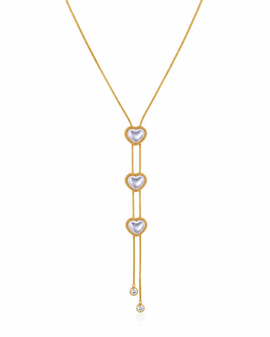 A gold Y-necklace featuring three vertical rows of heart-shaped pearl pendants, with a small clear crystal drop at the bottom, set against a plain white background.