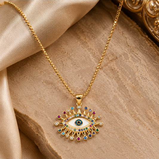 Gold-tone evil eye pendant necklace with a white enamel center and multicolored gem accents, displayed on draped beige satin fabric.