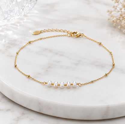 A delicate gold chain bracelet with five small white pearls and tiny gold beads, displayed on a white marble tray.