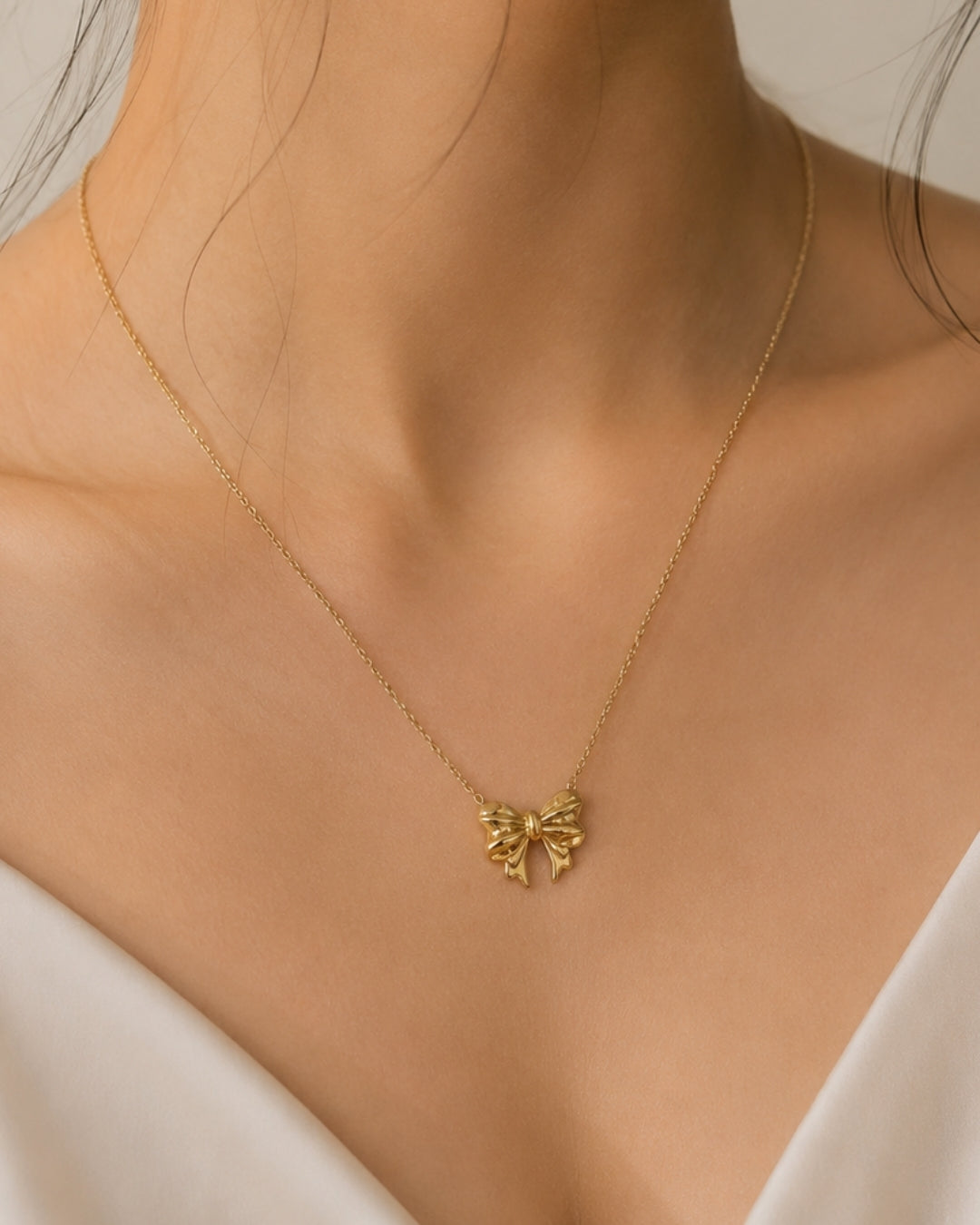 A delicate gold chain necklace with a small bow-shaped pendant, worn on a model's neck over a white top.