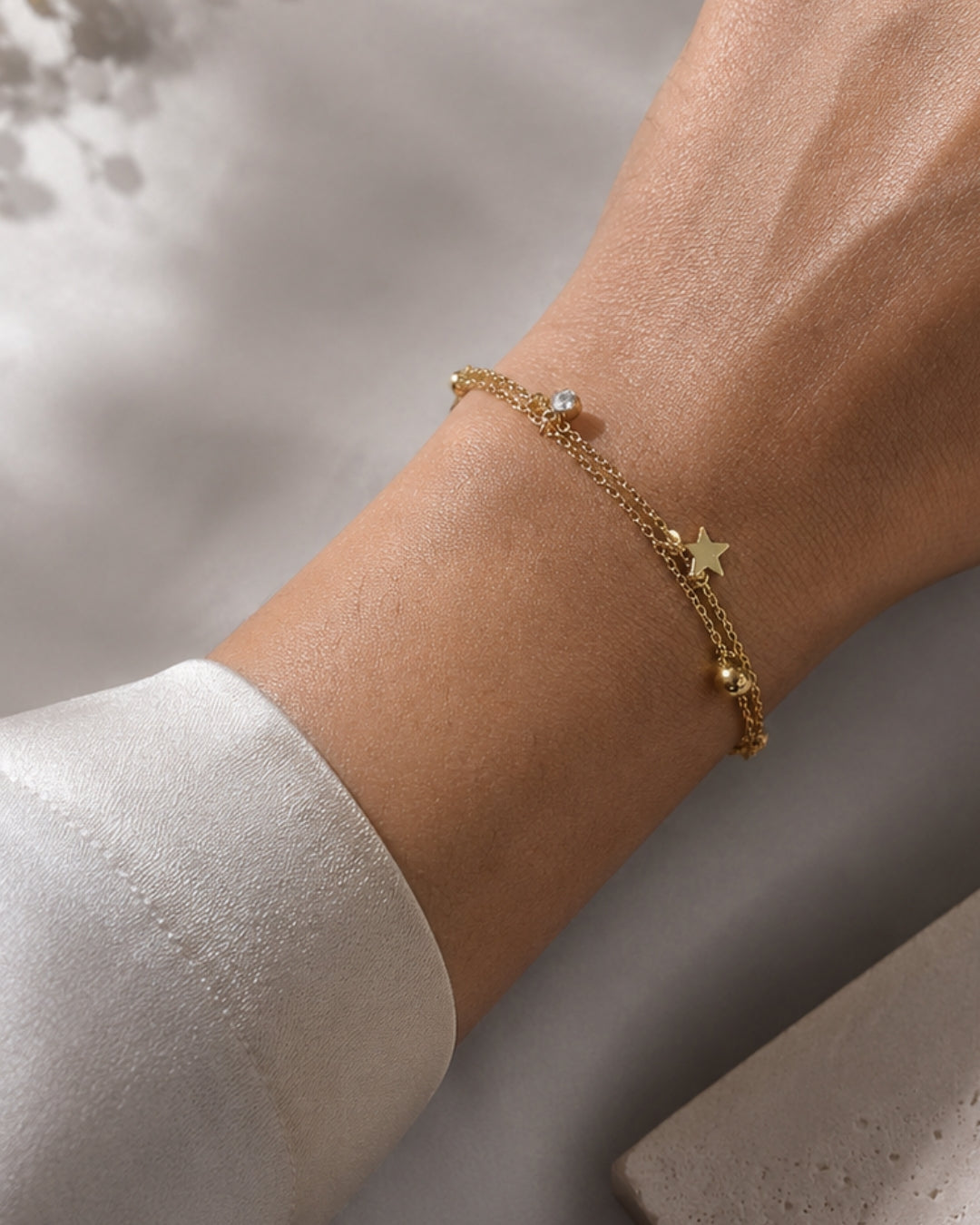 A delicate gold chain bracelet with a star charm and a small clear stone, shown worn on a person's wrist.