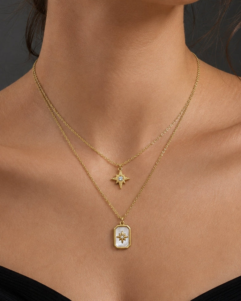 A close-up of a model wearing a delicate gold double-layer necklace with a small star pendant and a larger rectangular pendant featuring a white mother-of-pearl background and gold detailing.