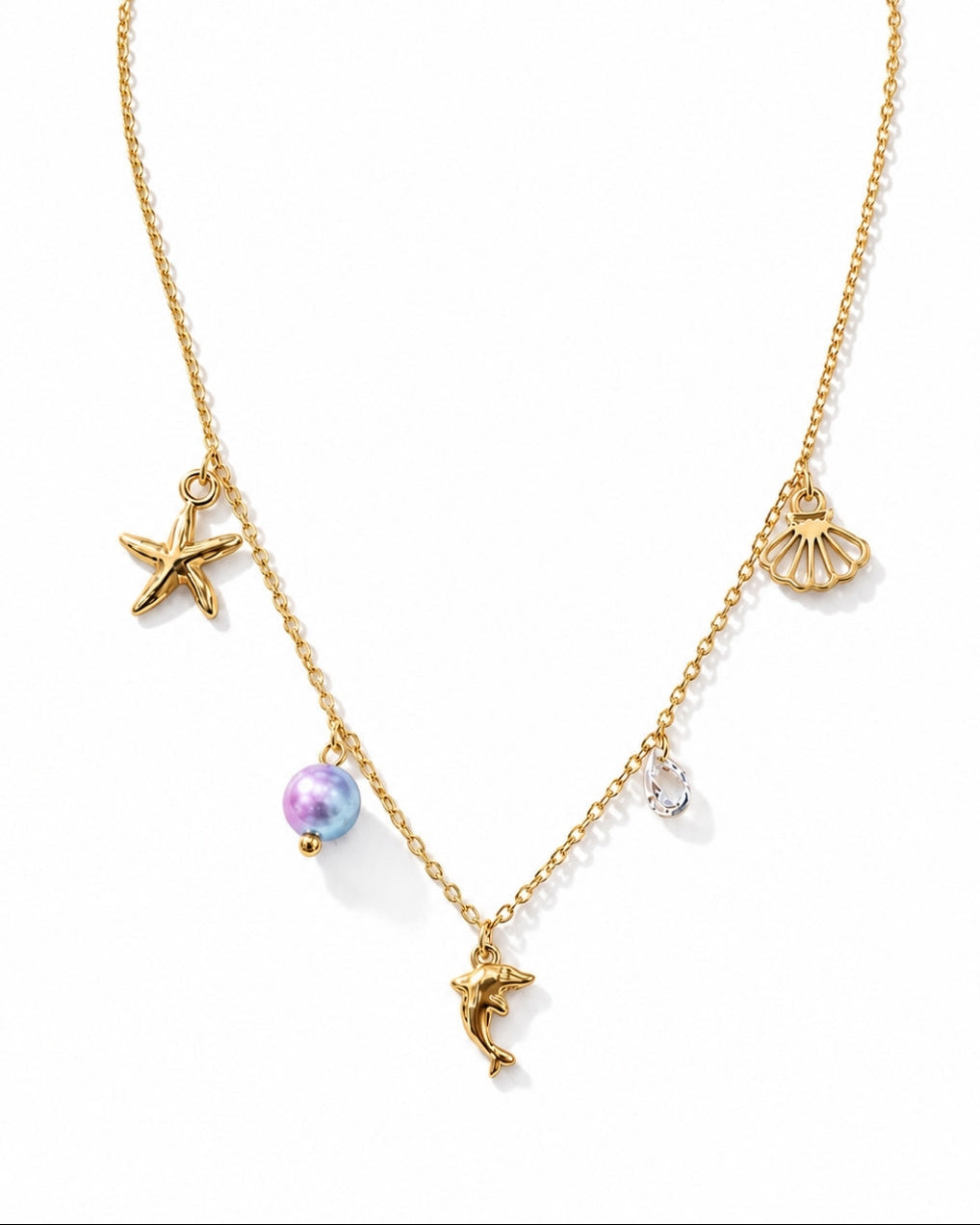 A gold chain necklace featuring sea-themed charms, including a starfish, a seashell, a dolphin, a pearl bead, and a small clear crystal charm, displayed on a clean white background.