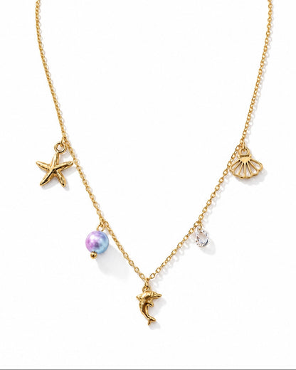 A gold chain necklace featuring sea-themed charms, including a starfish, a seashell, a dolphin, a pearl bead, and a small clear crystal charm, displayed on a clean white background.