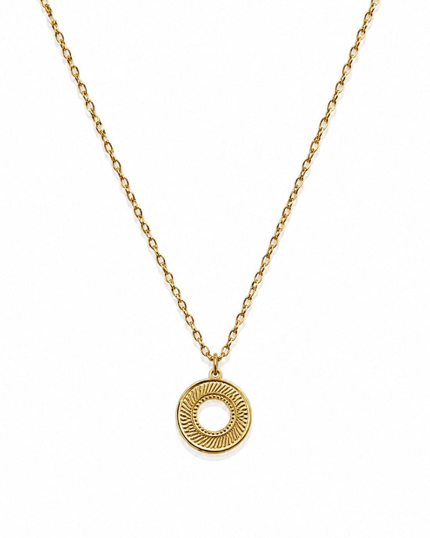 A gold chain necklace with a textured circular pendant featuring a sunburst pattern and a central cutout, displayed on a clean white background.