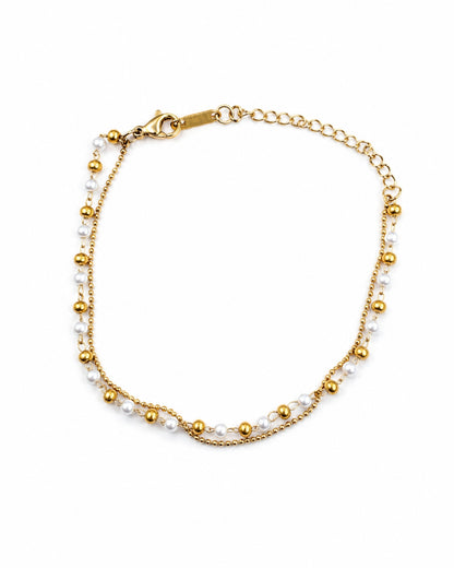A delicate gold chain bracelet featuring small white pearls and polished gold beads, displayed on a clean white background.