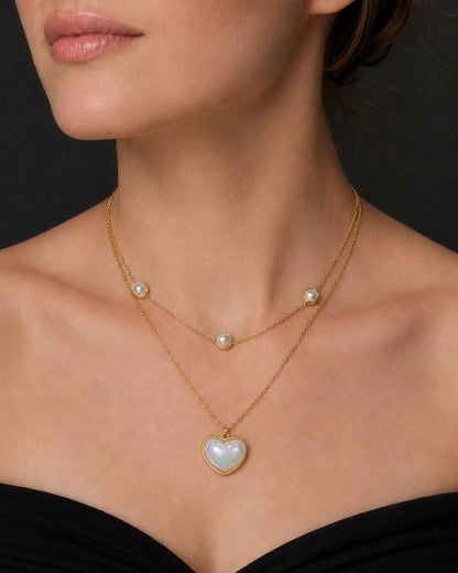 A close-up of a model wearing a delicate gold double-strand necklace with white pearl accents and a heart-shaped pearl pendant.