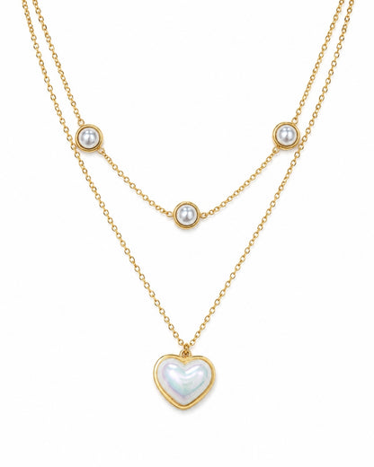 A double-layered gold necklace featuring a long chain with a heart-shaped iridescent pearl pendant and a shorter chain with three small round pearl beads, displayed on a clean white background.