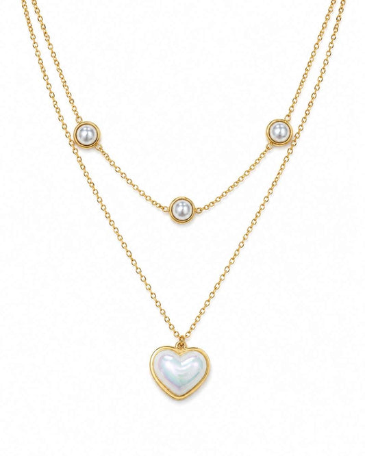 A double-layered gold necklace featuring a long chain with a heart-shaped iridescent pearl pendant and a shorter chain with three small round pearl beads, displayed on a clean white background.