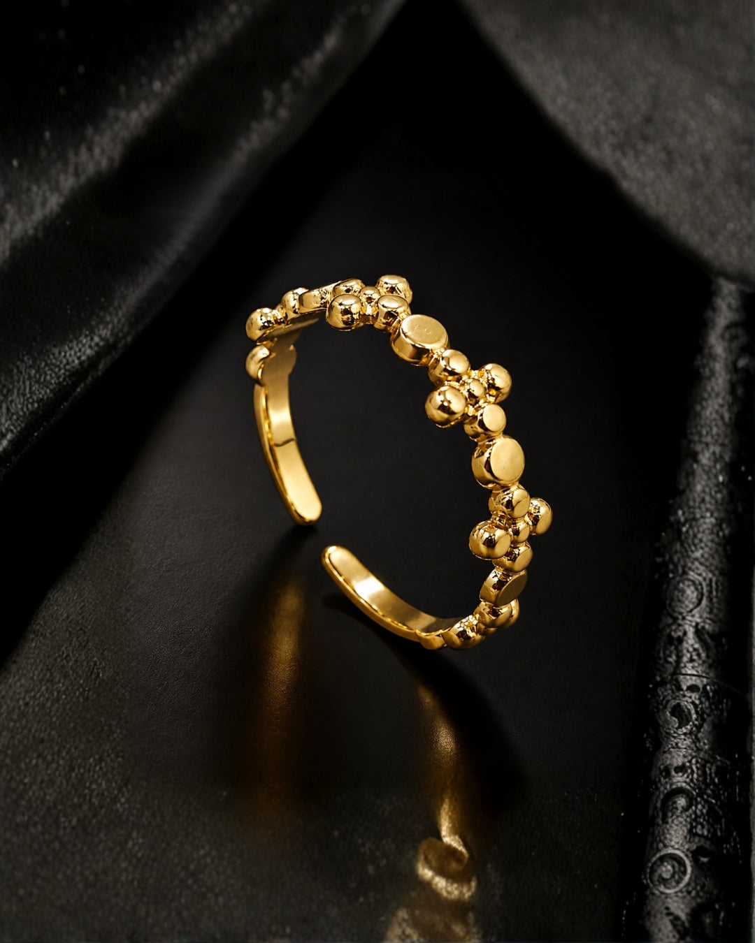 A gold adjustable ring with a textured, beaded floral pattern, displayed on a black satin surface.