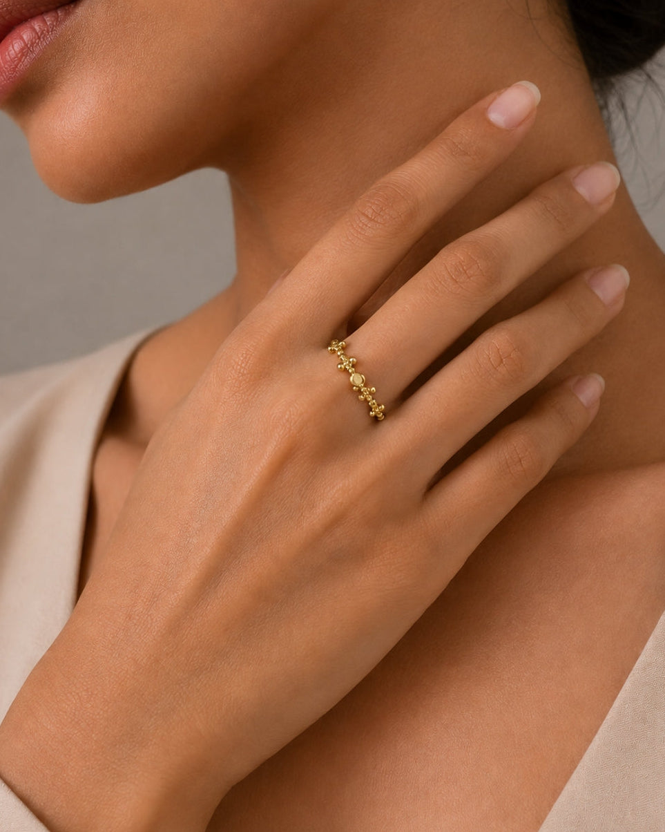 A close-up lifestyle shot of a model wearing a delicate gold ring with small, repeating floral or vine motifs on one finger.