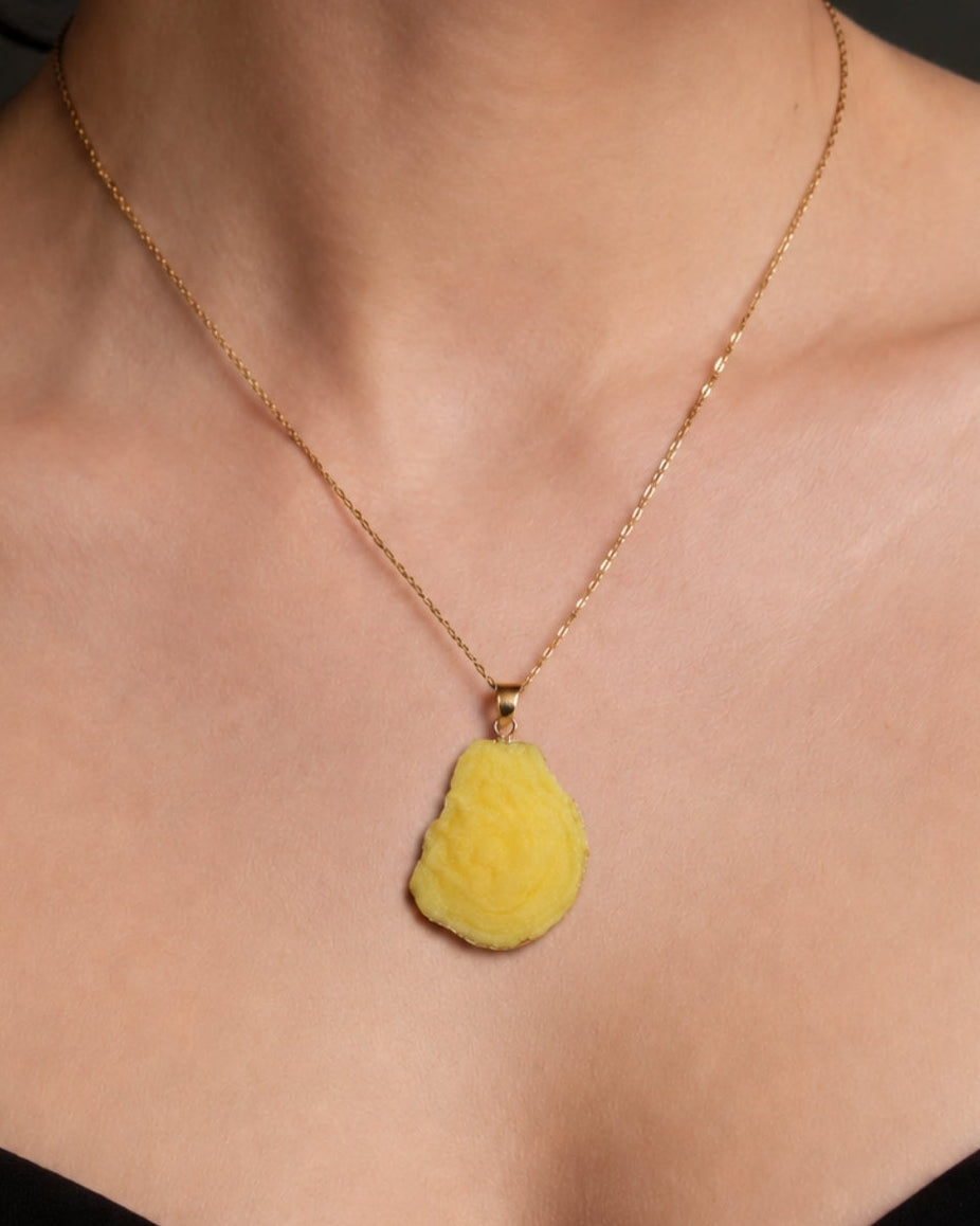 A close-up of a model's neck and chest wearing a delicate gold chain necklace with a textured, organic-shaped yellow pendant.