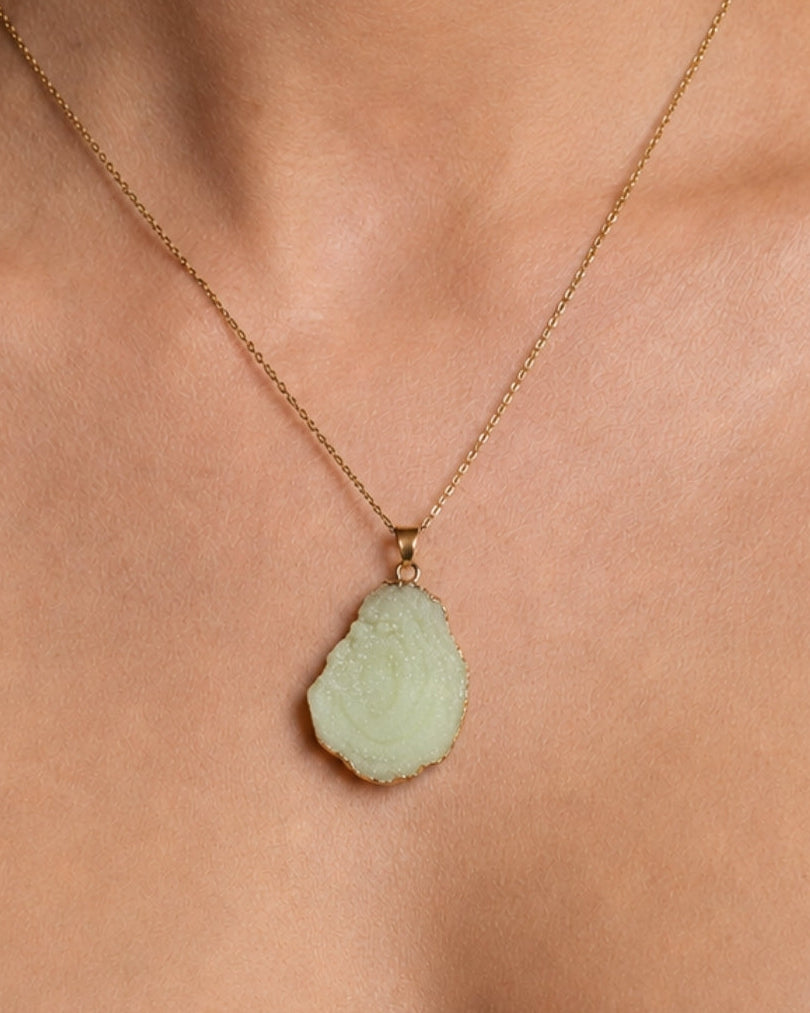 A gold chain necklace with a light green carved stone pendant, shown worn on a model's neck.