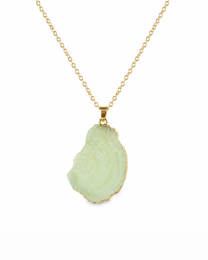 A gold chain necklace featuring a raw, irregular-shaped light green geode or druzy stone pendant with a gold border, shown against a plain white background.