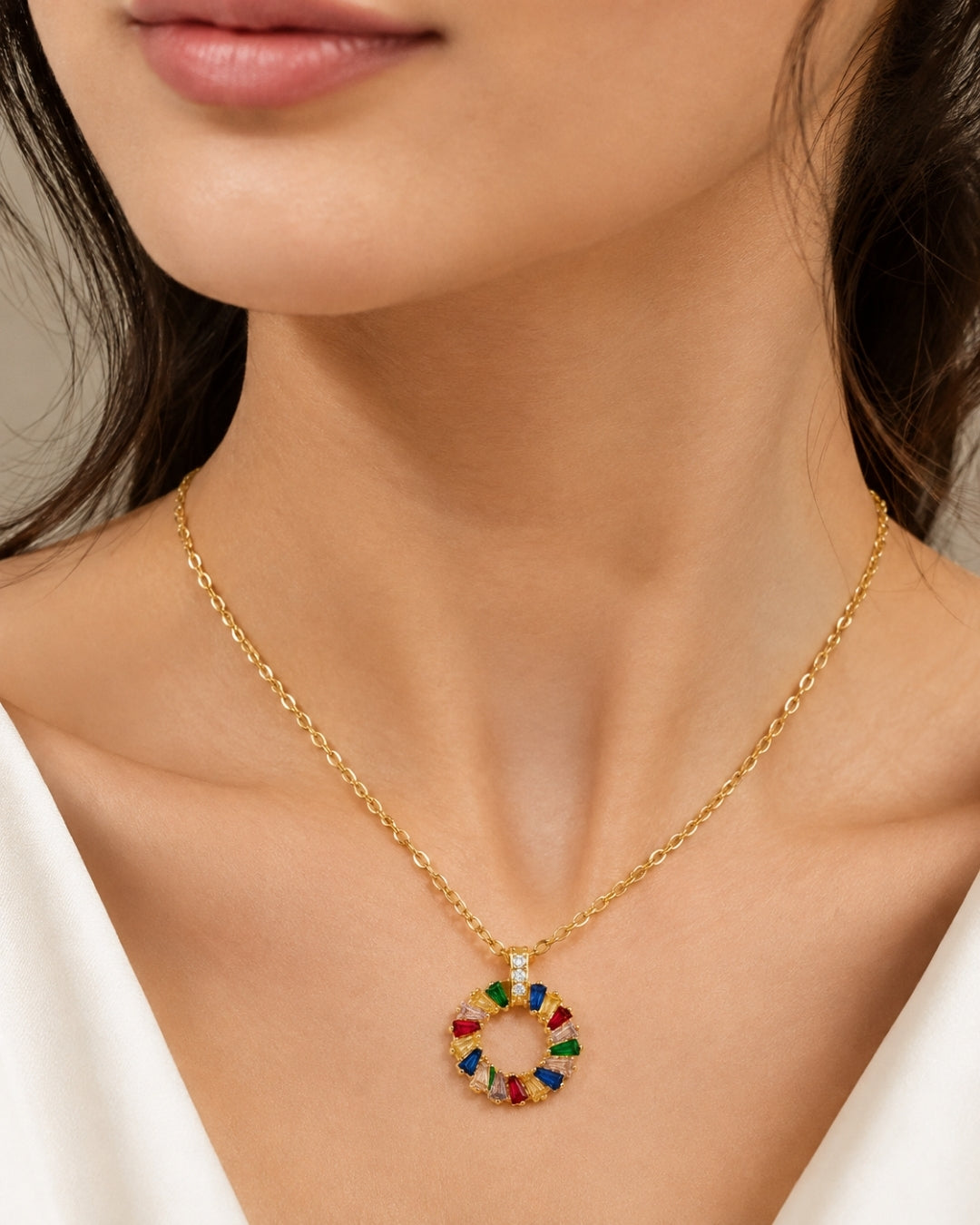 A close-up of a model wearing a gold chain necklace with a circular pendant featuring colorful, multi-toned segments.