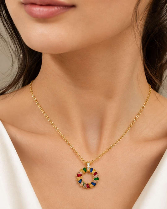 A close-up of a model wearing a gold chain necklace with a circular pendant featuring colorful, multi-toned segments.