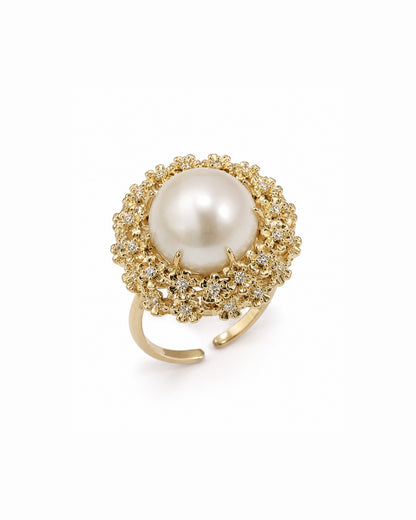 A gold-plated open-shank ring featuring a large, round white pearl surrounded by a halo of small clear crystals, set against a plain white background.