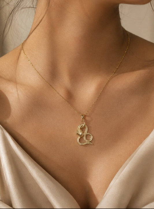 A close-up of a woman wearing a delicate gold chain necklace with a coiled snake pendant, styled with a satin cream top.