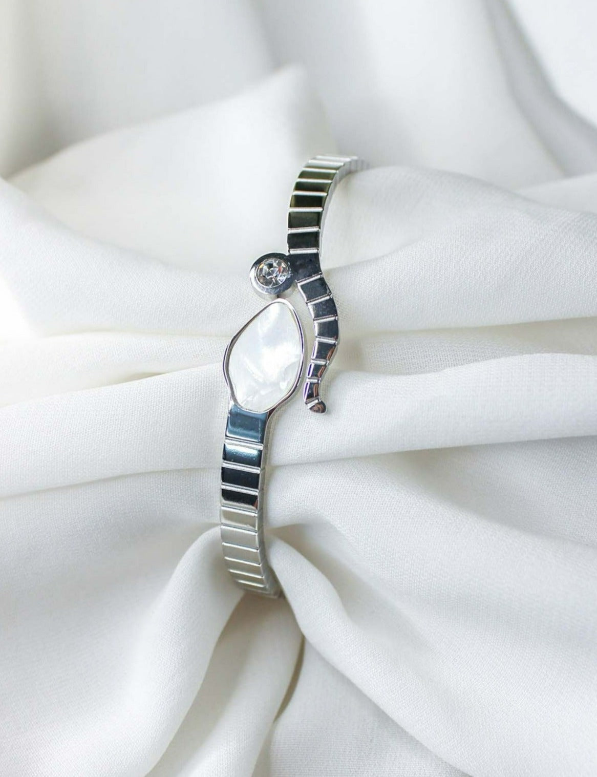 A sleek stainless steel snake bracelet with a mother of pearl embellished snake head on an open bangle, displayed on a white fabric surface.