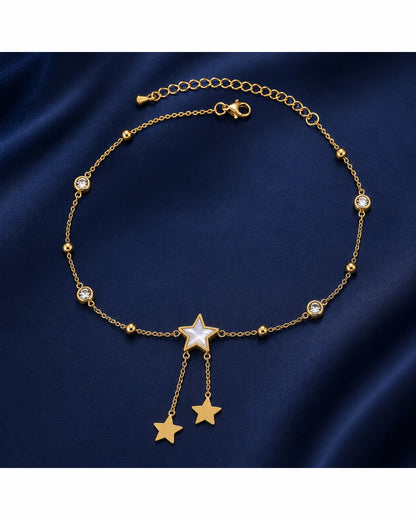 A gold-toned chain necklace with a central star charm, two dangling star charms, and small clear rhinestone accents, displayed on a dark navy satin fabric background.